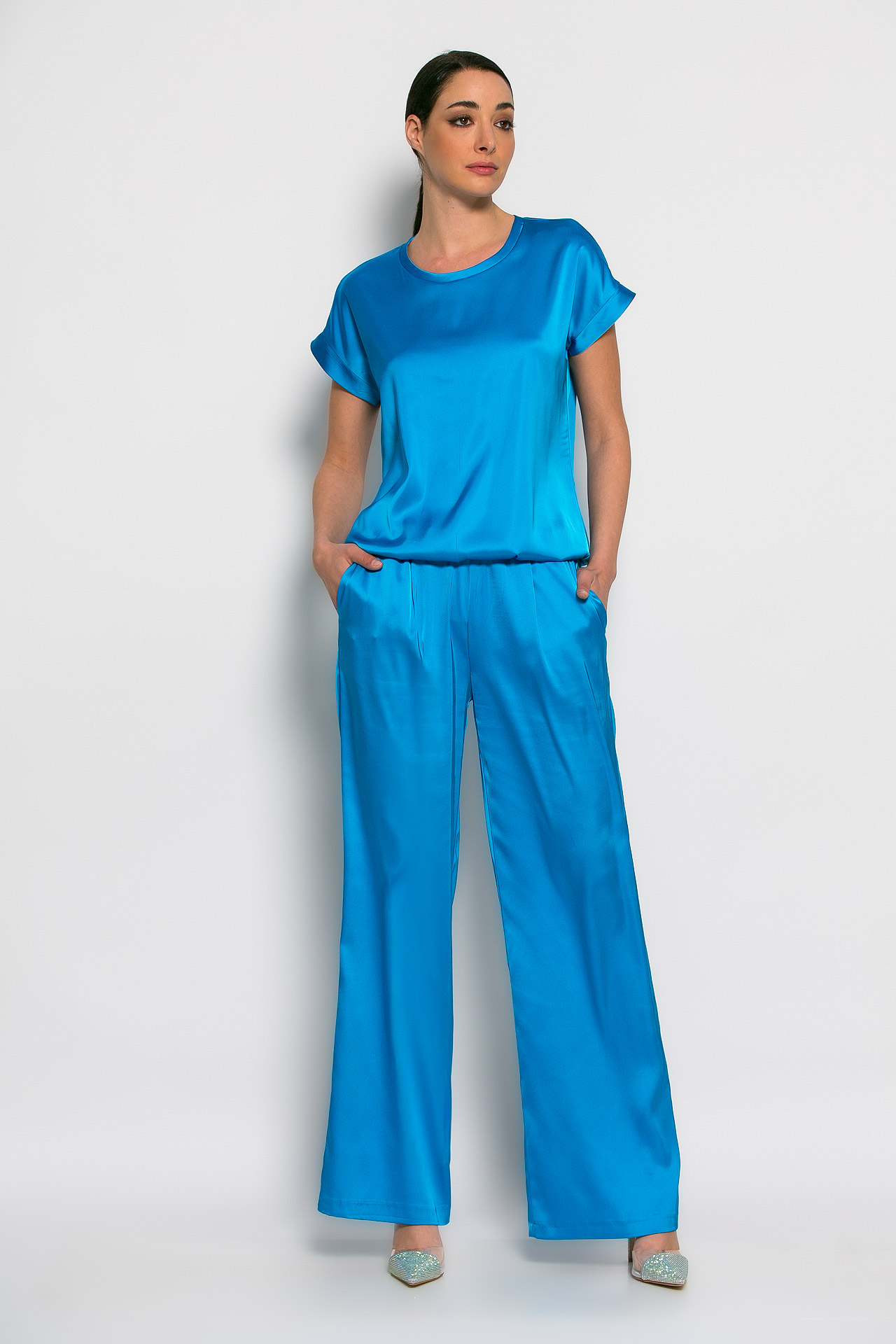 Studio still of a model wearing a cyan-blue satin two-piece outfit on an off-white backdrop